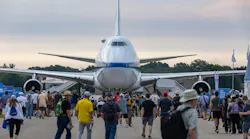 A large airplane sits on pavement surrounded by people walking on the ground around it