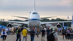 A large airplane sits on pavement surrounded by people walking on the ground around it A large airplane sits on pavement surrounded by people walking on the ground around it
