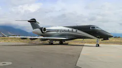 A black and white airplane with ornate stripe designs on the side sits on a tarmac with mountains and a blue sky behind it