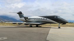 A black and white airplane with ornate stripe designs on the side sits on a tarmac with mountains and a blue sky behind it A black and white airplane with ornate stripe designs on the side sits on a tarmac with mountains and a blue sky behind it