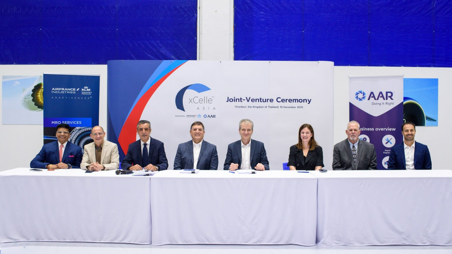 A group of professionals in business attire sit at a table on the same side, smiling at the camera and sitting in front of a backdrop that reads 'xCelle Asia Joint-Venture Company'