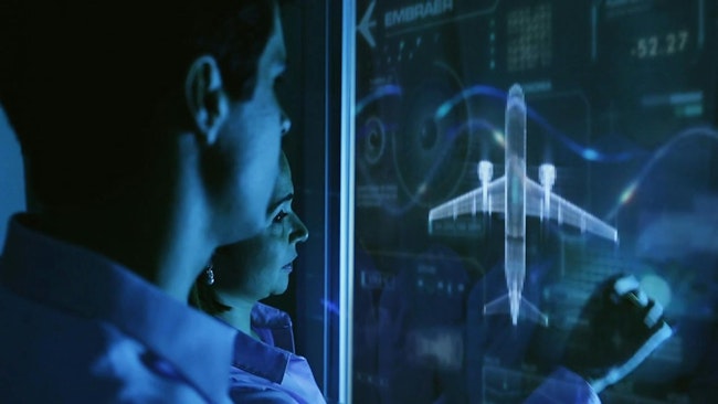 Two people in dim blue lighting look at an image of an airplane and data graphics on a large screen