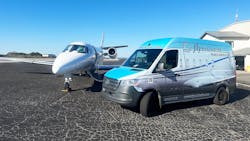 A chrome-colored van with text on it that reads 'flyExclusive' is parked next to a white jet plane on a tarmac A chrome-colored van with text on it that reads 'flyExclusive' is parked next to a white jet plane on a tarmac