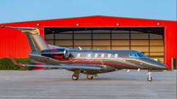 A dark gray aircraft with blue and red stripes sits on a tarmac in front of a red building A dark gray aircraft with blue and red stripes sits on a tarmac in front of a red building