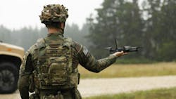 A person wearing military fatigues holds a drone in their hand A person wearing military fatigues holds a drone in their hand