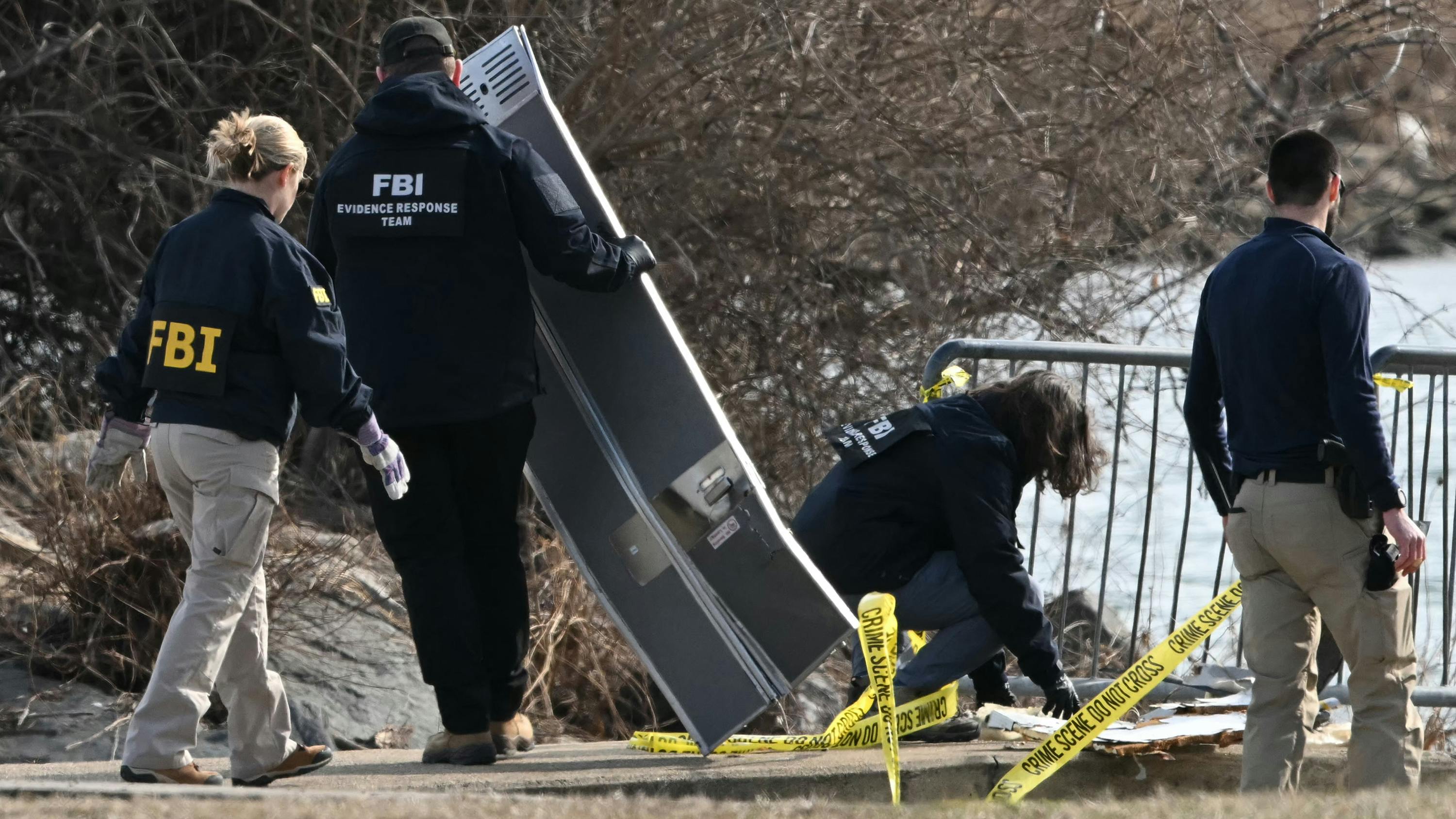 A group of people with 'FBI' on their sweatshirts investigates a pile of aircraft wreckage