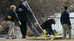 A group of people with 'FBI' on their sweatshirts investigates a pile of aircraft wreckage