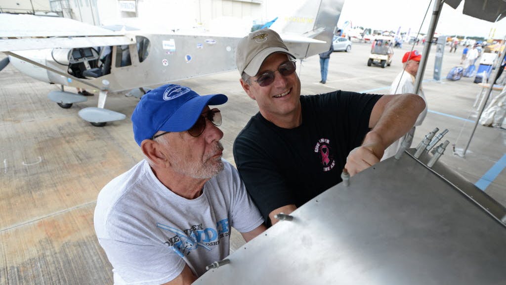 Two men work together on an aircraft's wing with another airplane behind them