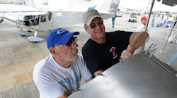 Two men work together on an aircraft's wing with another airplane behind them