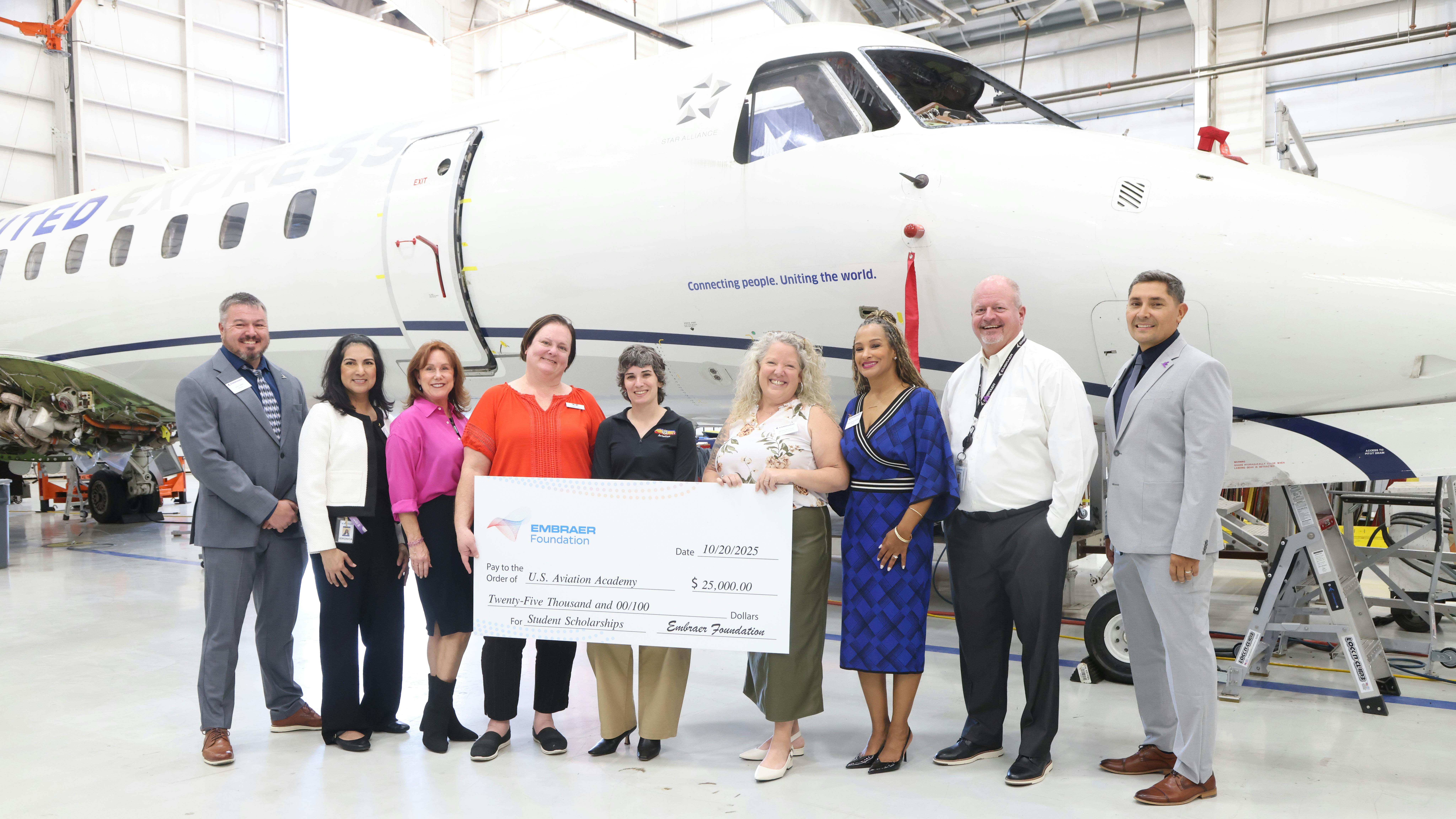 A group of people in business attire smile at the camera while holding a giant check and standing in front of a white airplane