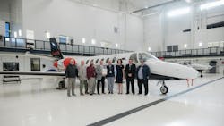 A group of professionals in business attire stand in front of an airplane in an airplane hangar, smiling at the camera A group of professionals in business attire stand in front of an airplane in an airplane hangar, smiling at the camera