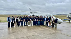 A group of professionals in business attire and AMT students in West Star Aviation Academy polos pose together in front of a white airplane