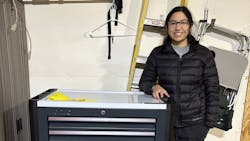 A woman wearing a black puffer jacket leans on a large upright toolbox and smiles at the camera A woman wearing a black puffer jacket leans on a large upright toolbox and smiles at the camera