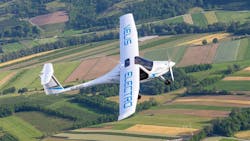 A white airplane featuring blue text that reads, 'VELIS ELECTRO' flies over rows of brown and green fields A white airplane featuring blue text that reads, 'VELIS ELECTRO' flies over rows of brown and green fields