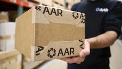 A person wearing a black shirt that says 'AAR' on it holding a shipping box with 'AAR' written on it close up to the camera A person wearing a black shirt that says 'AAR' on it holding a shipping box with 'AAR' written on it close up to the camera