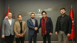Five men in professional attire stand smiling at the camera, with two men shaking hands in front of a wall sign that reads, 'Turkish Technic' Five men in professional attire stand smiling at the camera, with two men shaking hands in front of a wall sign that reads, 'Turkish Technic'