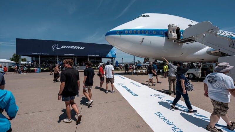 A wide shot of Boeing Plaza at EAA AirVenture, showcasing an airplane, a crowd of people and a building with the word 'BOEING' on it