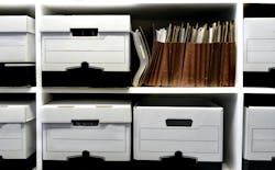A wall of shelves filled with banker boxes and file folders arranged in a haphazard way A wall of shelves filled with banker boxes and file folders arranged in a haphazard way