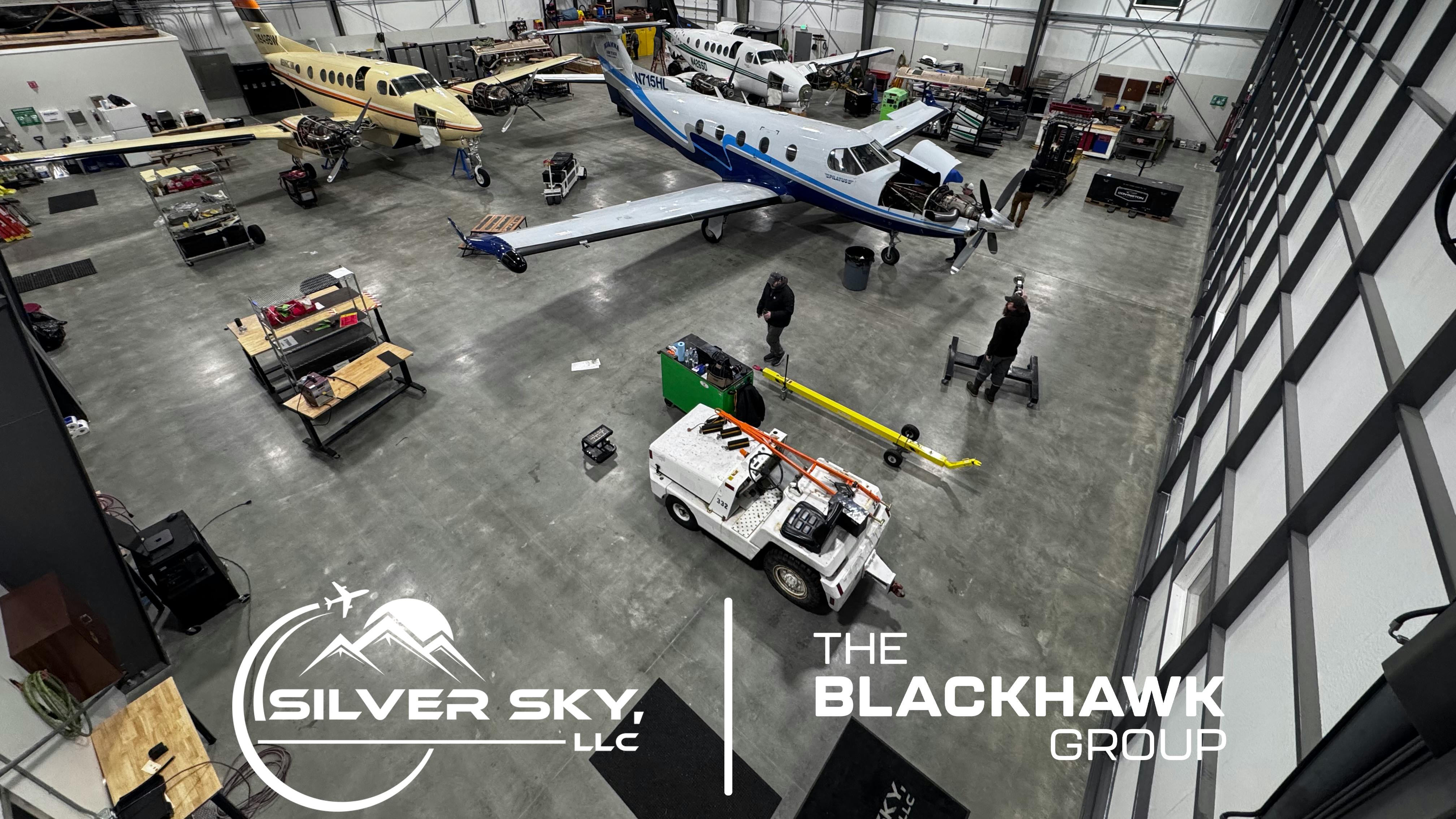 An overhead shot of a maintenance hangar with two airplanes and a variety of tug ground vehicles