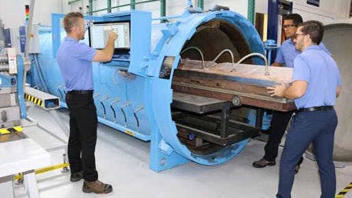 A group of aircraft mechanics in blue shirts working on an airplane part with a large piece of machinery