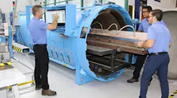 A group of aircraft mechanics in blue shirts working on an airplane part with a large piece of machinery