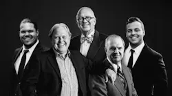 A black-and-white photograph of a group of men wearing suits and smiling at the camera