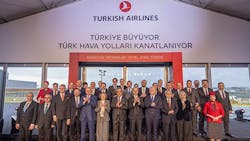 A large group of people wearing business attire stand in front of a building labeled 'Turkish Airlines' while smiling at the camera A large group of people wearing business attire stand in front of a building labeled 'Turkish Airlines' while smiling at the camera