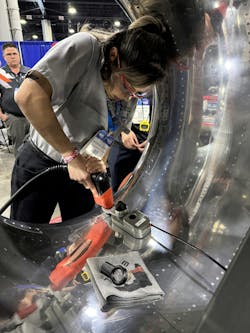 An aircraft maintenance technician using a tool on a shiny piece of metal equipment An aircraft maintenance technician using a tool on a shiny piece of metal equipment