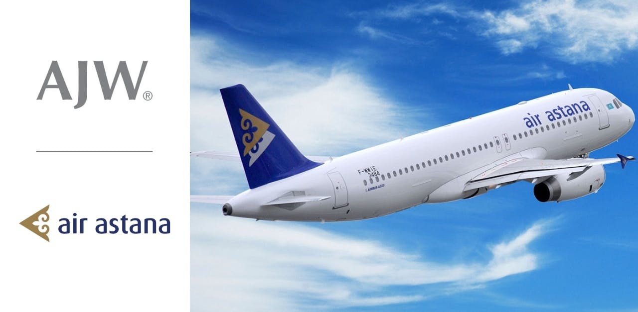 A white airplane flying against a blue sky next to two company logos that say, 'AJW Group' and 'Air Astana'