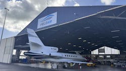 An aircraft hangar with the door open and an airplane parked halfway inside, with a sign on the front of the building that reads: FIELDAIR An aircraft hangar with the door open and an airplane parked halfway inside, with a sign on the front of the building that reads: FIELDAIR