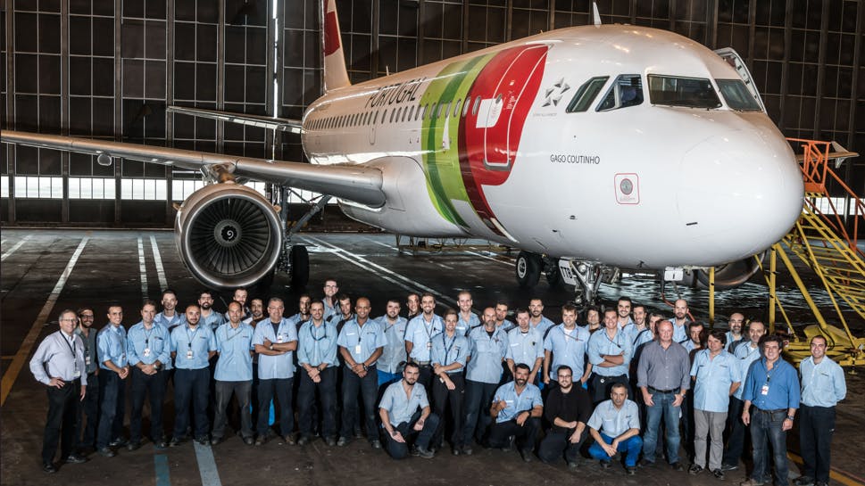 A large group of aviation maintenance technicians wearing blue shirts standing in front of an airplane