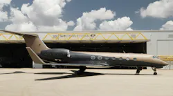 A black and tan airplane parked in front of an aircraft hangar with a sign on it that reads: VIP Completions