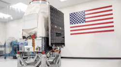 A Saturn-200 minisatellite sitting in a white room with an American flag behind it