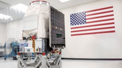 A Saturn-200 minisatellite sitting in a white room with an American flag behind it A Saturn-200 minisatellite sitting in a white room with an American flag behind it