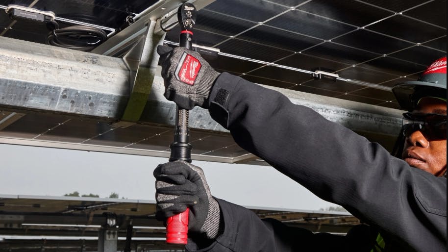 A man wearing a black sweatshirt and protective glasses and gloves holding a large wrench