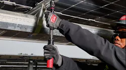 A man wearing a black sweatshirt and protective glasses and gloves holding a large wrench