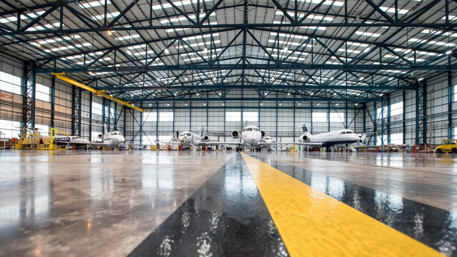 A wide shot of an aircraft maintenance hangar with a shiny brown, black, and yellow floor and four airplanes sitting inside