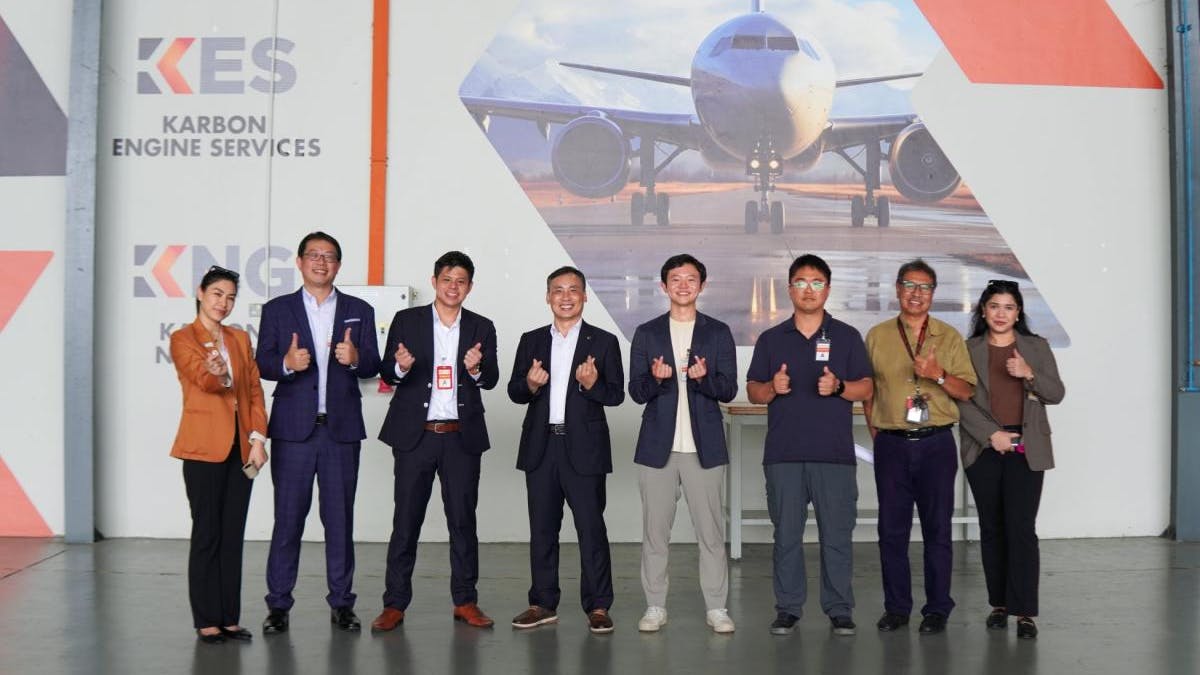 A group of people in business attire making thumbs-up and heart hand gestures while standing in front of a large photo of an airplane
