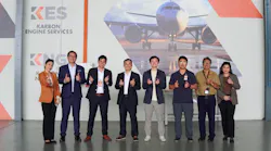 A group of people in business attire making thumbs-up and heart hand gestures while standing in front of a large photo of an airplane