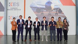 A group of people in business attire making thumbs-up and heart hand gestures while standing in front of a large photo of an airplane A group of people in business attire making thumbs-up and heart hand gestures while standing in front of a large photo of an airplane