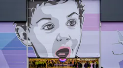 A large hangar door with a mural painted on it, showcasing a child's face and an airplane off to the side in shades of gray, blue and purple
