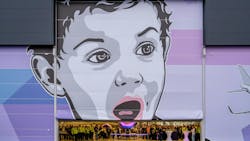 A large hangar door with a mural painted on it, showcasing a child's face and an airplane off to the side in shades of gray, blue and purple A large hangar door with a mural painted on it, showcasing a child's face and an airplane off to the side in shades of gray, blue and purple