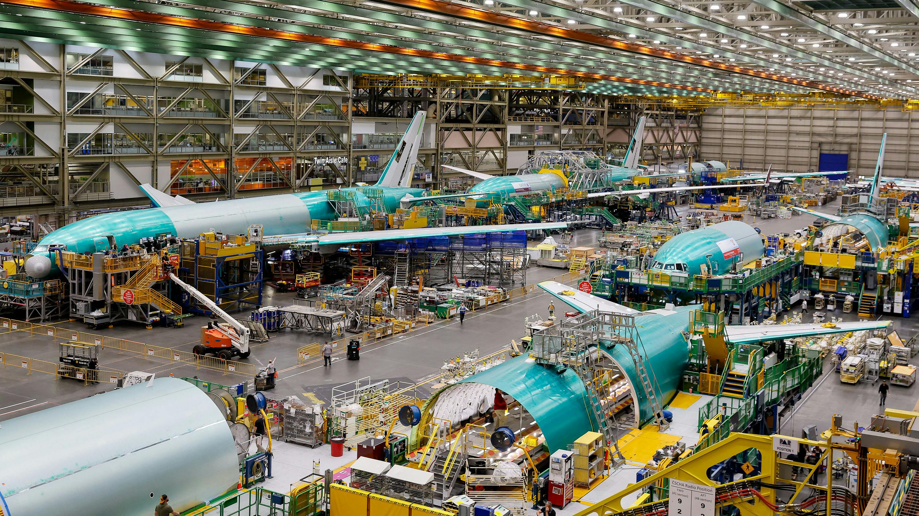 A hangar showing airplanes and machinery with people working around the machines