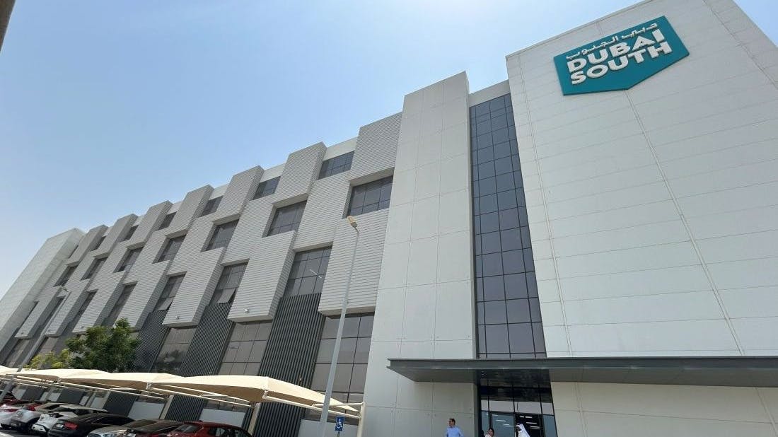 The exterior of a building with white brick and dark glass with a sign on the front that reads: DUBAI SOUTH