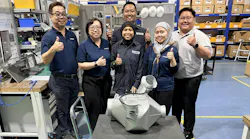 A group of maintenance technicians smiling at the camera with some giving a thumbs-up hand gesture, all standing behind an aircraft component in a repair shop