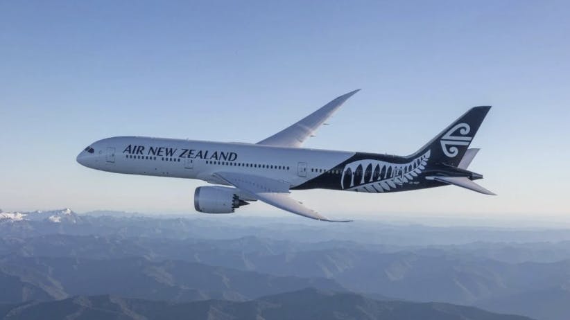 A white airplane with decorative designs on the tail and text on the side that reads: Air New Zealand