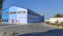 A building painted in three shades of blue across the street from a warehouse with a sign on it that reads 'AkzoNobel' slightly blocked by trees A building painted in three shades of blue across the street from a warehouse with a sign on it that reads 'AkzoNobel' slightly blocked by trees