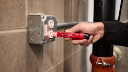 A hand holding a red hand tool, touching it to an electrical outlet as the tool emits a red light A hand holding a red hand tool, touching it to an electrical outlet as the tool emits a red light
