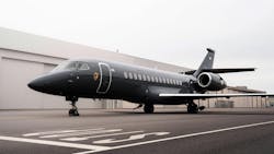 A large black airplane on a tarmac in front of beige buildings A large black airplane on a tarmac in front of beige buildings