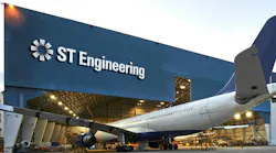 An airplane parked halfway into a maintenance hangar that has a sign on the front reading: ST Engineering